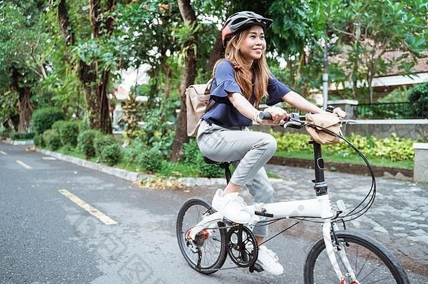 亚洲年轻女子戴着头盔和包骑着她的折叠自行车