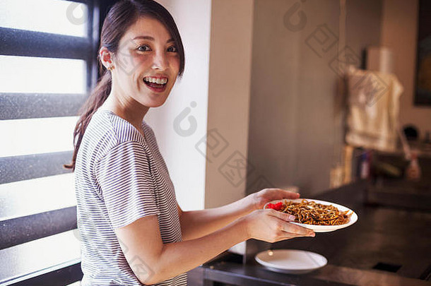一名女子在一家面馆里拿着一盘苏巴面条。
