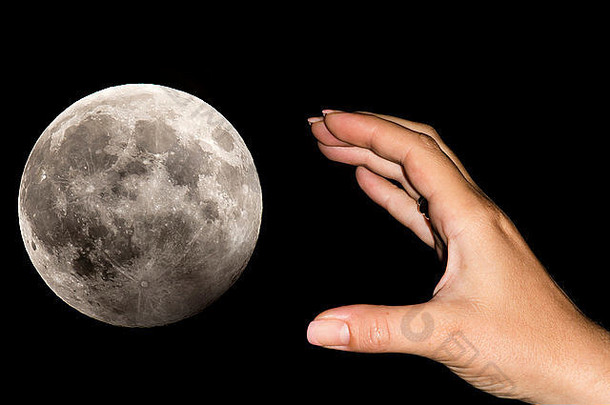 一个女人的手正把月亮举过黑色的天空。抱负、白日梦、不可能的事情的概念形象