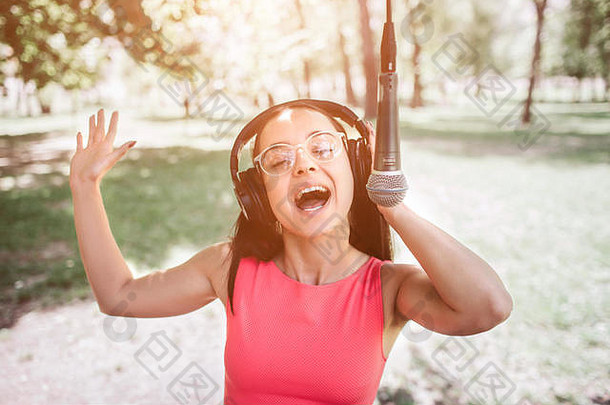 情绪化的女孩戴着耳机听音乐的照片。她还在公园外面对着麦克风唱歌。她很享受