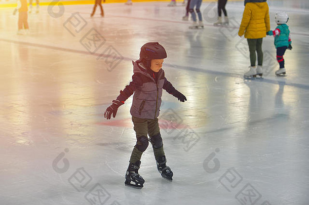 穿着冬衣，带着保护装置的可爱小男孩在溜冰场上滑冰