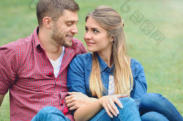 一对浪漫的情侣坐在草地上看着对方的眼睛。爱、关系、家庭和人的概念