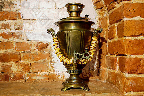 在俄罗斯红砖烤箱的墙壁背景上，古代的铜萨莫瓦尔以羊肉制品装饰的形式矗立着。背景，r