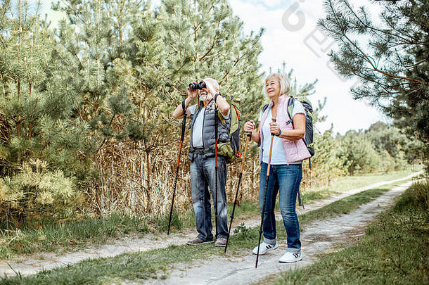 在森林里徒步旅行时，一对幸福的老年夫妇带着望远镜、背包和<strong>登山杖</strong>站在一起。退休后积极生活方式的概念