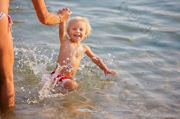 快乐儿童的夏日和游泳活动。孩子跳进水里，开心地笑着，溅起水花，妈妈牵着他的手