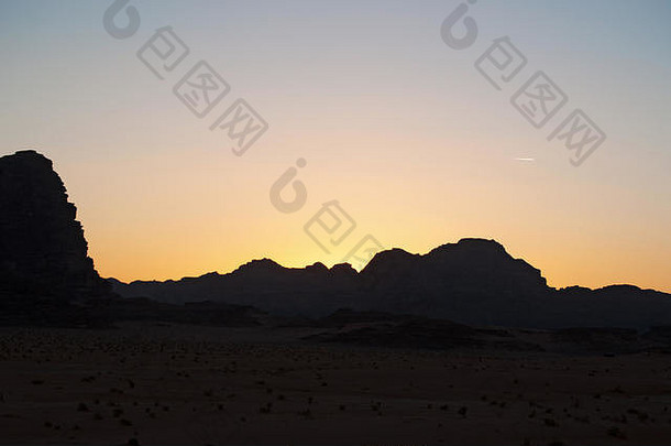 在瓦迪拉姆沙漠（Wadi Rum desert）的一座山的黑暗轮廓上，火红的日落，这是一个著名的月球山谷，看起来像火星