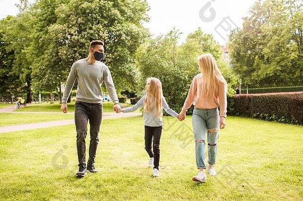 在公园散步的家庭成员戴着织物面罩。父亲、母亲和女儿<strong>保护自己</strong>免受病毒感染