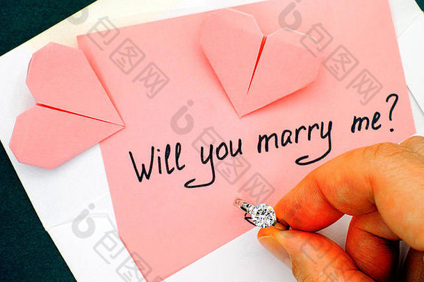 手持订婚戒指的女人。有文字的信你愿意嫁给我吗？信封里，桌子上放着两颗折纸心形。