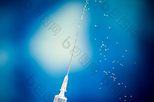 蓝色背景前有疫苗液体流动的注射器。特写镜头。医学、科学和保健概念