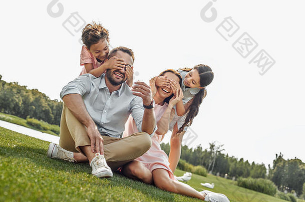 猜一猜快乐年轻的家庭微笑有趣的坐着草公园野餐周末
