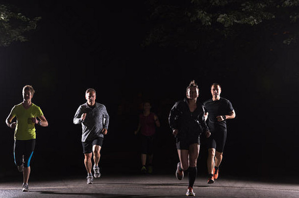 一群健康的人在城市公园慢跑，跑步队在夜间训练