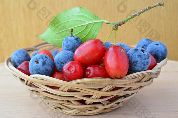 木质背景上的柳条篮中混合了营养和疗效、新鲜和成熟的山茱萸和黑刺或树莓，近景