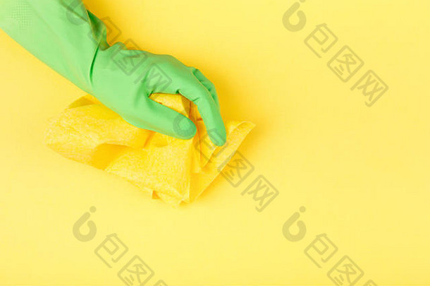 交上绿色橡胶防护手套，黄色背景上有黄色抹布。清洁概念。