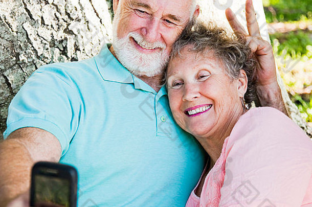 可爱的老年夫妇用手机拍摄他们的自画像。他在给她打兔子耳朵。