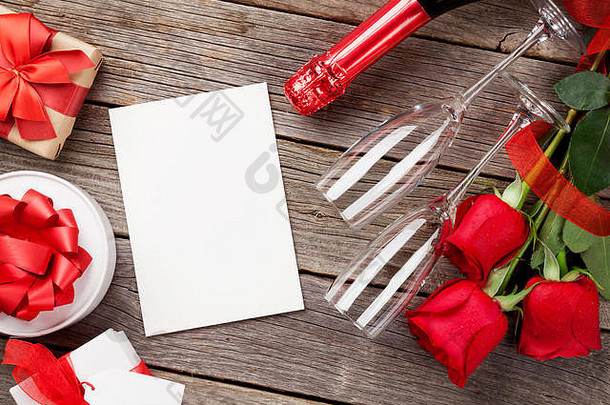 红玫瑰、礼品盒、香槟和木制背景上的空白贺卡。具有空间的俯视图