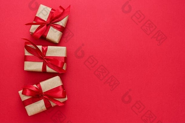 用<strong>牛皮纸包装</strong>的礼品盒和红色背景上隔离的红结。抽象平铺。