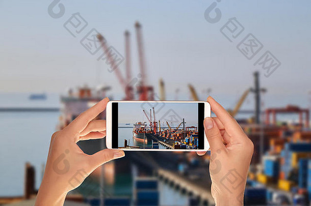 一名游客正在拍摄意大利集装箱码头的照片，码头上的起重机正在装载一艘大型货船。进出口物流