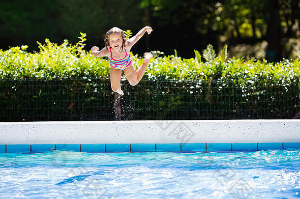 家庭暑假期间，一个快乐的小女孩跳进了热带度假胜地的室外游泳池。孩子们学习游泳。
