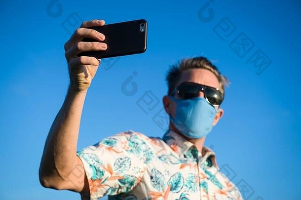 穿着色彩鲜艳的夏威夷衬衫、戴着防护面罩的游客站在户外进行检疫自拍