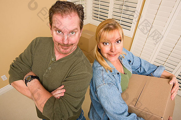 一对傻乎乎的夫妇微笑着，在空房间里搬箱子。