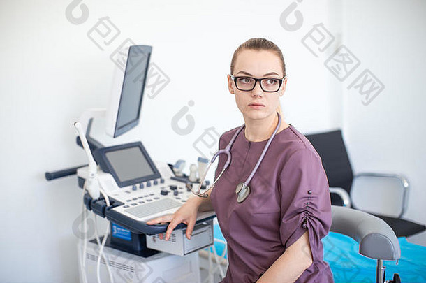 在超声波机附近的诊所里，一位身穿Purple制服的金发女<strong>医生</strong>戴着眼镜，脖子上戴着听诊器