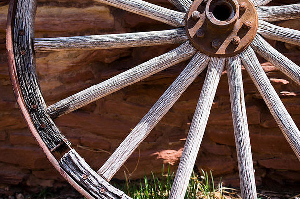 在一堵石墙的背景下，一个生锈的金属轮圈和带螺栓的轮毂的旧木制车轮的细节