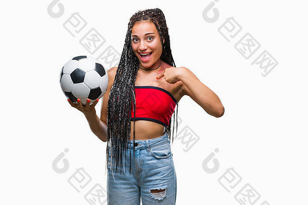 年轻的辫发非洲裔美国人，有出生标记，在孤立的背景下拿着足球，惊讶地用手指着自己