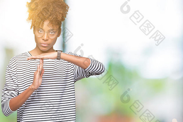 一位年轻漂亮的非裔美国妇女戴着眼镜，在与世隔绝的背景下用手做着暂停的手势，沮丧而严肃的脸