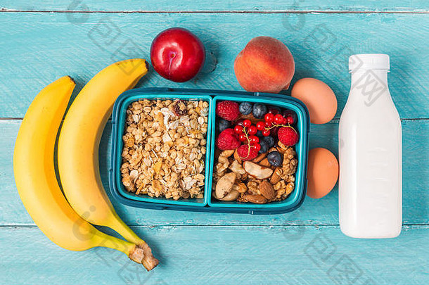 学校午餐盒子格兰诺拉麦片坚果浆果香蕉鸡蛋桃子酸奶使早餐蓝色的背景前视图复制空间