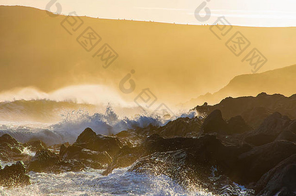 英国南威尔士海岸的金色日落。飞溅的波浪和晚风，悬崖和薄雾的背景。英国风景名胜区。海滩上的神奇时刻。