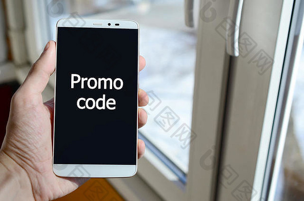 一个人在手里拿着的黑色智能手机显示屏上看到一个白色的铭文。促销代码。