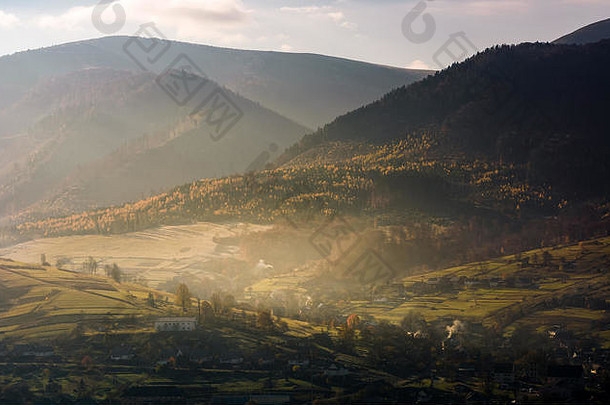 多雾的秋天日出在山区农村地区。美丽的山脊上有着黄树的村庄和森林