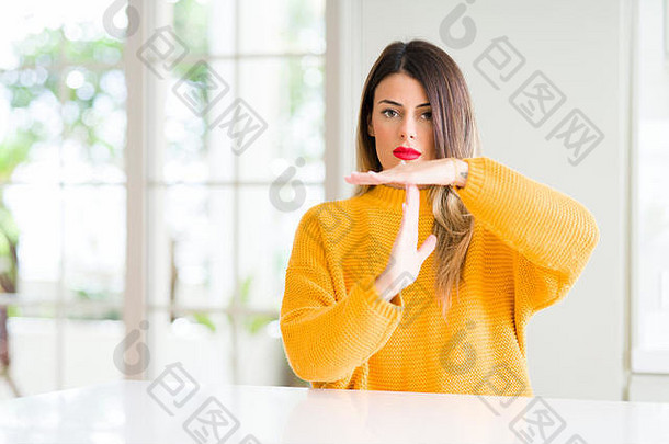 年轻漂亮的女人穿着冬天的毛衣在家做着超时的手势，用手，沮丧而严肃的表情