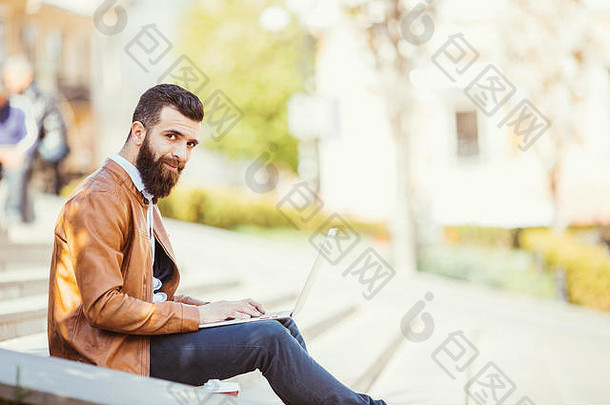 一个英俊的年轻人坐在楼梯上的笔记本电脑旁，一边打电话