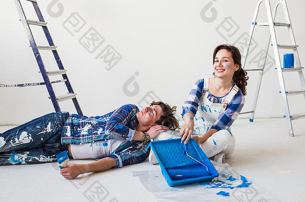 一对微笑的恋人正在装修房子。年轻的女人拿着一个油漆辊，年轻的男人在休息