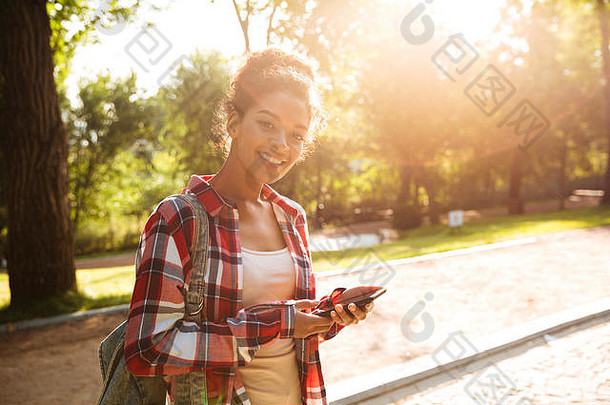 令人惊叹的非洲年轻女子在公园户外行走的画面。看着摄像机，通过电话<strong>聊天</strong>。