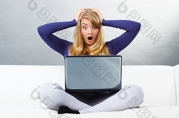 震惊、惊讶和恐惧的女人双手捂着头，坐在沙发上，看着笔记本电脑屏幕，电脑出现问题，