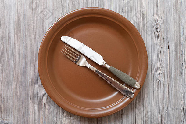 食物概念-灰褐色桌子上带平行刀、汤匙的棕色盘子俯视图