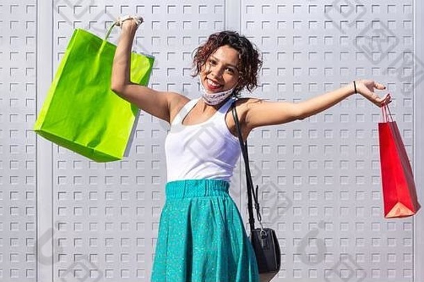 这位年轻的女士在一家购物中心外举起她的购物袋，高兴地微笑着。全景图。文本的空间。安全购物概念。