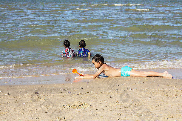 亚裔泰国男孩在沙滩上玩，兄弟姐妹坐在水里看海