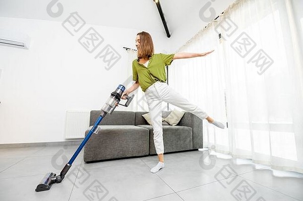 年轻女子喜欢做家务，在现代化的白色客厅里用无绳吸尘器清洁地板。使用无线吸尘器轻松清洁的概念