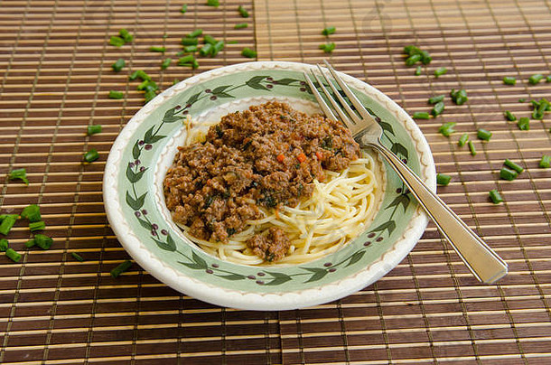 碗里的意大利面，肉酱，叉子放在竹垫上，洋葱