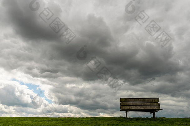 在阴雨密布、乌云密布的弗里斯兰河堤上的长凳。荷兰