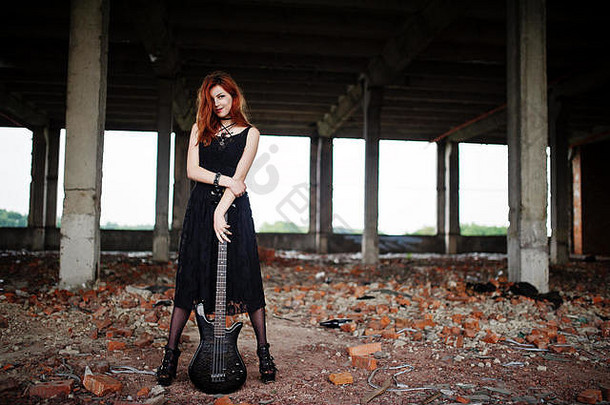 红头发的朋克女孩穿着黑色的衣服，在阿巴登的地方弹奏低音吉他。哥特式女音乐家的肖像。