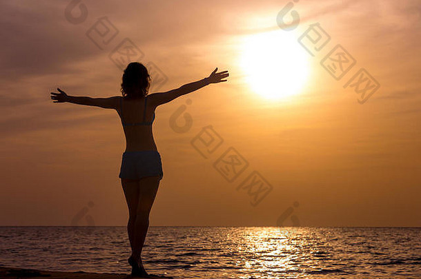 年轻快乐的女人伸开双臂站<strong>在海边</strong>，沐浴<strong>在</strong>温暖的阳光下，看着五颜六色的日出