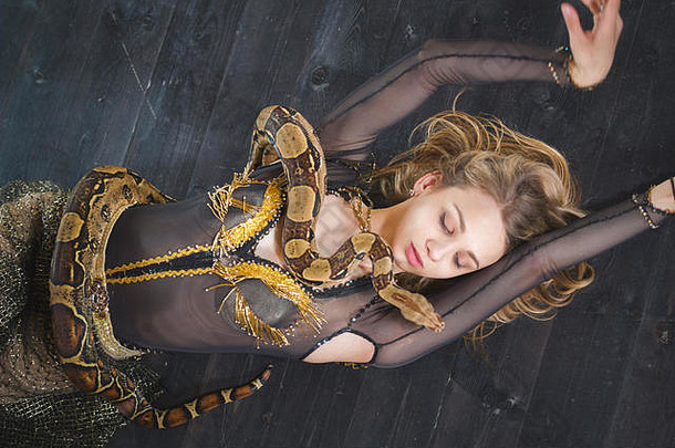 漂亮的年轻女子躺在地板上，身上有一条蛇