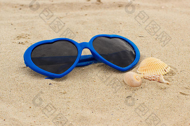 蓝色有趣的太阳镜，心形和贝壳状，躺在沙滩上，假期和夏天，保护眼睛