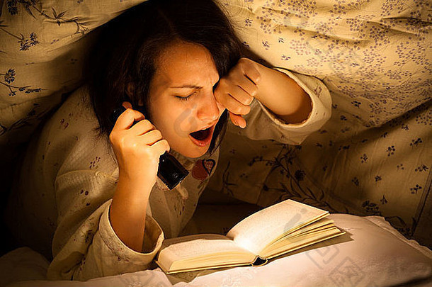 打呵欠女人阅读书手电筒床上
