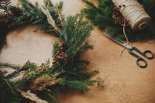质朴的圣诞花环。冷杉枝，松果，线，浆果，木桌上的剪刀。圣诞花圈工作坊。真实时尚的静物画。