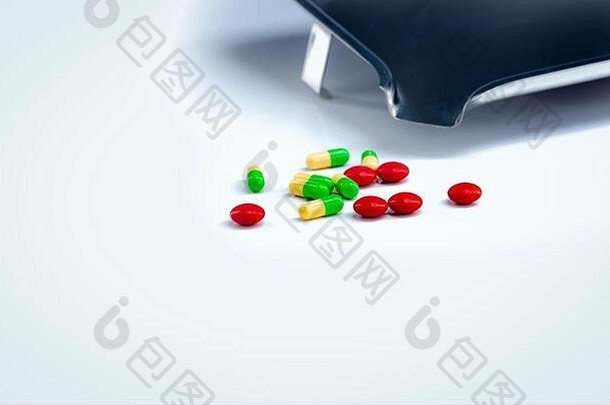红色药片和绿黄色胶囊药片，白色桌子上有药盘。制药业。维生素和补充剂。药剂学概念。
